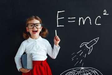 Child girl prodigy student with book near blackboard