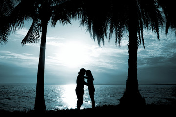 silhouette couple, woman and man standing and will kissing in front of the sea have coconut tree shadow, look love , so sweet and romantic, blue shade style