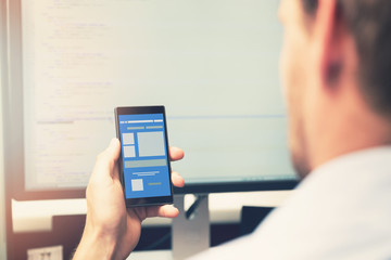 Wall Mural - mobile app development - smart phone with application wireframe in programmer hand