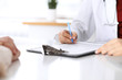 © rogerphoto - Close up of a female doctor filling up  an application form while consulting patient