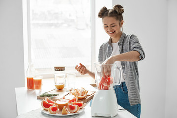 Positive young girl cutting grapefruit blending healthy detox fresh smoothie over white wall.