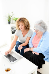 Wall Mural - mature woman helping at home assisted elderly senior female buying and shopping online on internet with a laptop computer and credit card