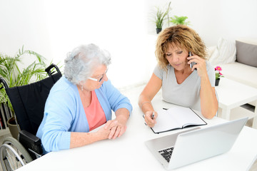 Wall Mural - mature woman helping assisted elderly senior female with administrative procedures and paperwork on internet with a laptop computer at home