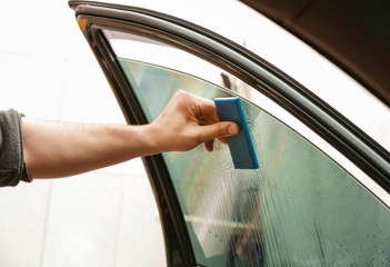 Worker applying tinting foil onto car window