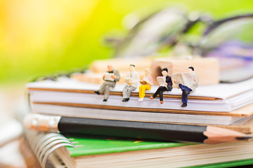 Miniature people sitting on pencil on book using as background education or business concept