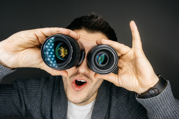 Portrait of a male photographer who holds two lenses near the eyes. Funny facial expression