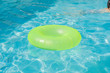 Bright green float in blue swimming pool, ring floating in a refreshing blue swimming pool with waves reflecting in the summer sun. Active vacation background. Lifesaver for kid. Sunny day at the pool
