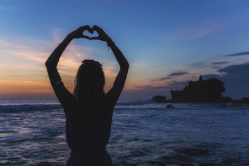 Girl holding a heart shape on the ocean / sea shore.