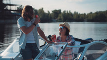Young Couple Toasting Each Other With Cans Of Beer As They Relax In The Evening On A Lake In A Motorboat While Enjoying Their Summer Vacation.