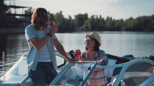 Cuadros en Lienzo Young couple toasting each other with cans of beer as they relax in the evening on a lake in a motorboat while enjoying their summer vacation