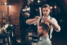 Profile View Of A Red Bearded Stylish Barber Shop Client. He Is Getting His Perfect Trendy Haircut From A Classy Dressed Handsome Stylist, Looking In A Mirror And Waiting For Result