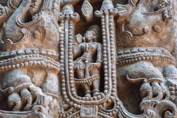 Wall Mural - Figure of lonely woman in Indian tradition on carved stone wall of Hindu temple. Ancient artwork of old religious structures in Halebidu, India.