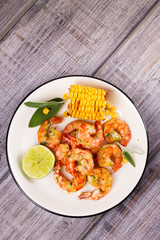 Wall Mural - Grilled shrimps and corn garnished with lime and sage leaves. Prawns on white plate. View from above, top studio shot