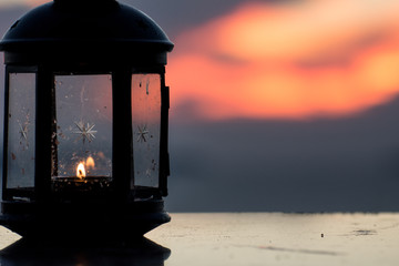 Lantern with burning candle glowing on the table with sea and sunset background