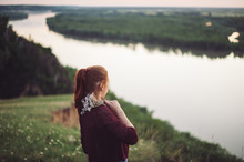 The Girl Is Standing With Her Back In The Field Against The Background Of The River, Nature.