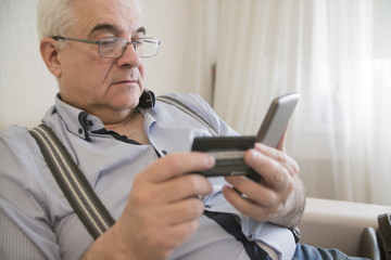 close-up adult gray-haired man holding a credit card and phone, it makes electronic payment