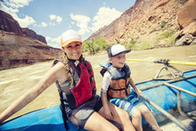  Cute Active Young Family Enjoying A Day Rafting Down A Whitewater River Together. The Mother And Son Sitting Together On A Large Raft Floating Down A Red Rock Canyon