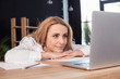 © LIGHTFIELD STUDIOS - Smiling blonde businesswoman looking at laptop while sitting at wooden table