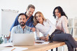 © LIGHTFIELD STUDIOS - Smiling business colleagues using laptop while sitting together at workplace