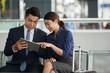 © DragonImages - Portrait of two Asian business people, man and woman,  using digital tablet while waiting in airport departure zone travelling on business trip