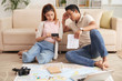 © DragonImages - Portrait of young Asian couple planning vacation sitting on floor at home with maps and calculator