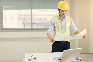 Handsome engineer holding blueprint and checking in the office.