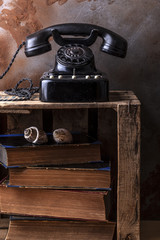 Dusty vintage bakelite phone on a wooden fruit box with old books and sea shells.