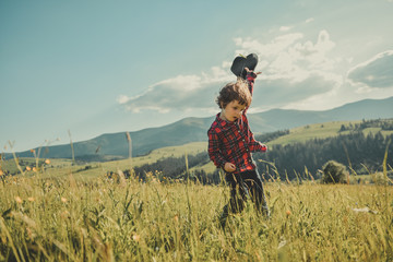 Happy little boy running over the top of the mountain. A child with a hat in his hand on a hill of the mountain. Carpathian mountains