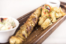 Pork Skewers Served With Baked Potatoes, Coleslaw Salad And Barbecue Sauce, Decorated With Radish, Red And Green Herbs, Placed On A Wooden Plate, Light Background, Isolated