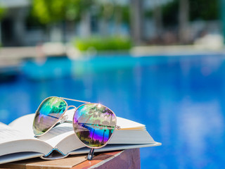 sunglasses on open book at the side of swimming pool. Vacation, beach, summer travel concept