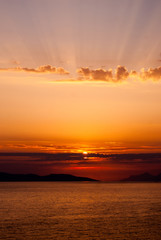 Wall Mural - panoramic image of golden sunset with sun low above the sea and sunrays coming through clouds above