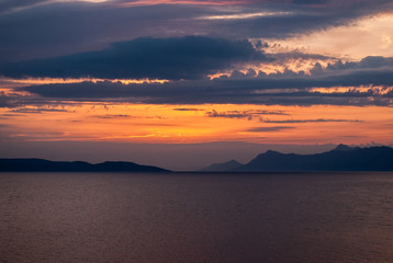 Wall Mural - Horizontal image of deep coloured sunset with blue, purple and golden hues, black mountains on the horizon,