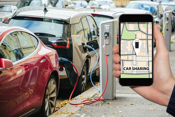 Hand with phone on a background of electric cars charging points. Car sharing concept