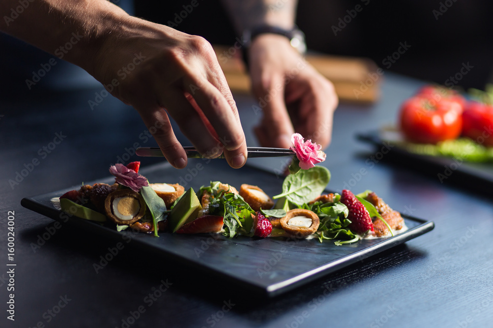Chef sprinkling spices on dish in commercial kitchen - obrazy, fototapety, plakaty 