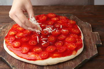 Wall Mural - Female hand making tasty traditional pizza on wooden board