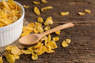 white bowl of cornflakes on sackcloth with wooden spoon on wooden background ,still life , in concept breakfas