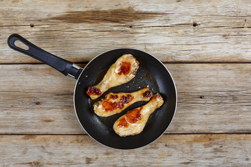 Wall Mural - Chicken grilled legs. Fried chicken legs in a frying pan on a wooden table, top view