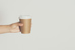 Womans hand holding brown paper cup of hot coffee.