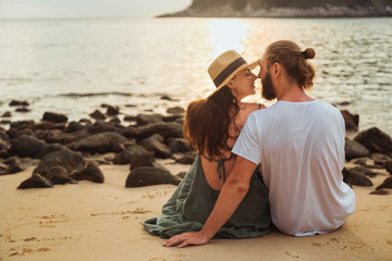 Lovers boy and girl are sitting on the shore of a tropical beach in the evening in the rays of the setting sun. A love story on vacation. Romantic date.