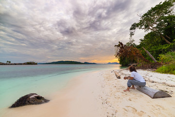 Wall Mural - Tourist watching a relaxing sunset sitting on the beach in the remote Togean Islands, Central Sulawesi, Indonesia, upgrowing travel destination in recent years. Wide angle view.