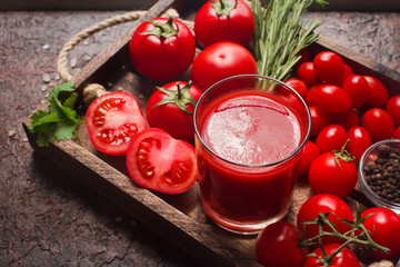 glass of tasty organic tomato juice and fresh tomatoes and herbs on wooden tray in rustic style. Selective focus, healthy lifestyle