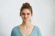 © WHstudio Leushin N - Indoor shot of blue-eyed pretty brunette woman making grimace blowing her cheeks having pleased expression. Beautiful young woman with pure healthy skin dressed in casual clothes being offended