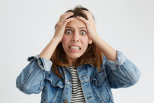 Portrait Of Shocked Terrified Woman With Dark Eyes Popped Out Clenching Her Teeth Holding Hands On Head Looking In Despair Into Camera Isolated Over White Background. Woman Having Frustration