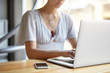 © WHstudio Leushin N - Cropped view of businesswoman sitting at wooden desk indoors surrounded with modern gadgets. Clever woman working online via laptop computer typing report. Woman's hands keyboarding on computer