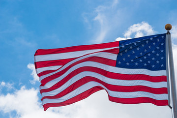 Large American flag waving on flag pole with cloud blue sky. Windy and sunny day with waving star and striped flag blowing/flowing. Ruffled USA flag. Room for text.