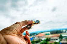 Man Playing Gold Fidget Spinner On Blur Top View Background