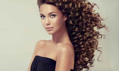 Brunette girl with long and shiny curly hair . Beautiful model with wavy hairstyle . 