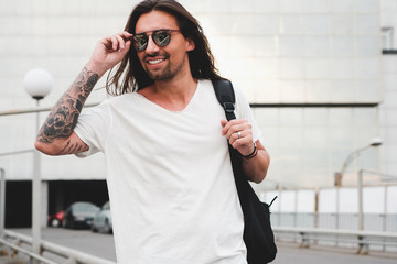 Stylish hipster model with long hair lifestyle in the street. Dressed in a white T-shirt and torn blue jeans in the city