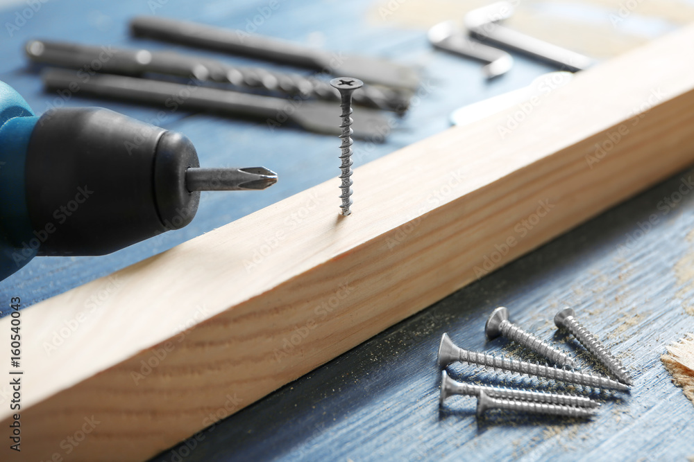 Wooden bar, screw nails and drill on table in carpenter's workshop, closeup