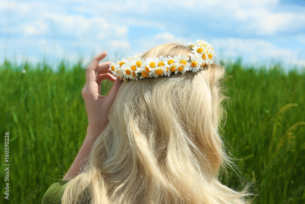 Beautiful young woman with chamomile wreath in field